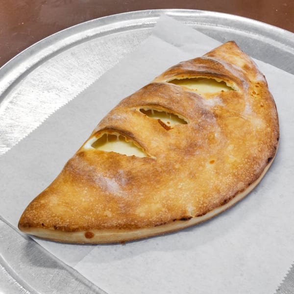 A golden-brown calzone with three slits revealing melted cheese, on parchment paper and a metal tray.