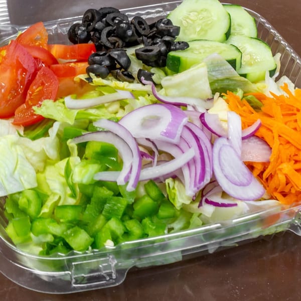 Fresh garden salad with lettuce, tomatoes, olives, cucumbers, onions, and carrots in a plastic container.