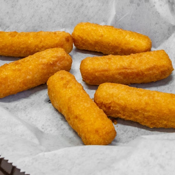 Six golden-brown fried mozzarella sticks are arranged on white parchment paper in a basket.
