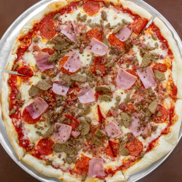 A Carini's Pizza with pepperoni, ham, and sausage, on a metal pizza pan.