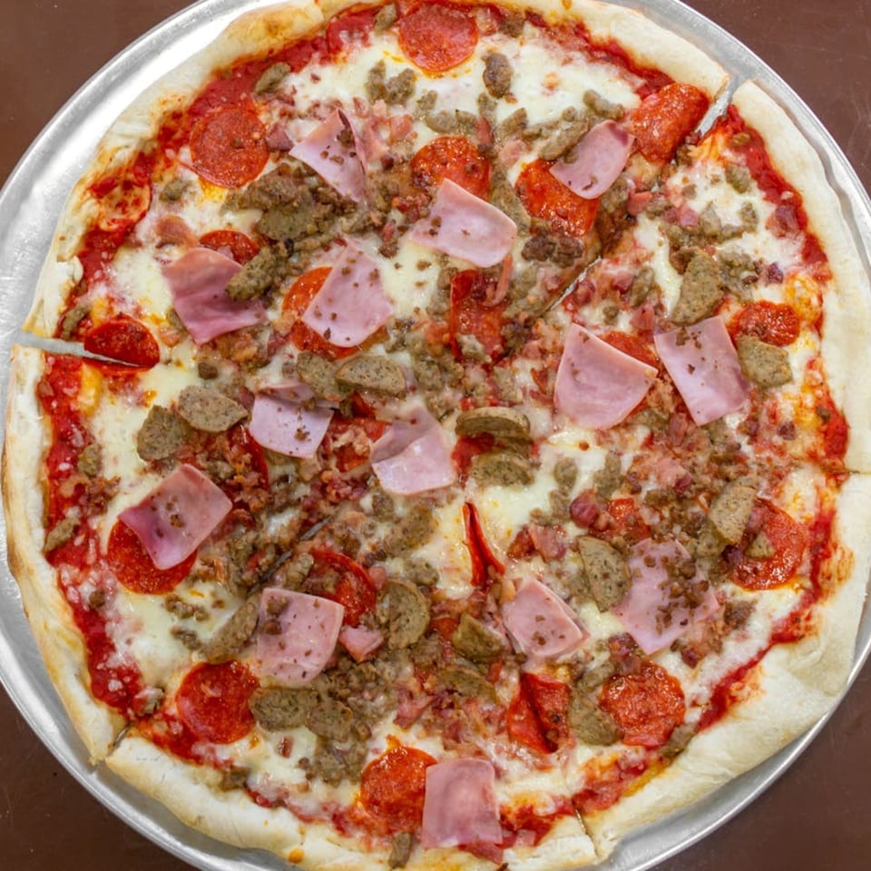 A Carini's Pizza with pepperoni, ham, and sausage, on a metal pizza pan.