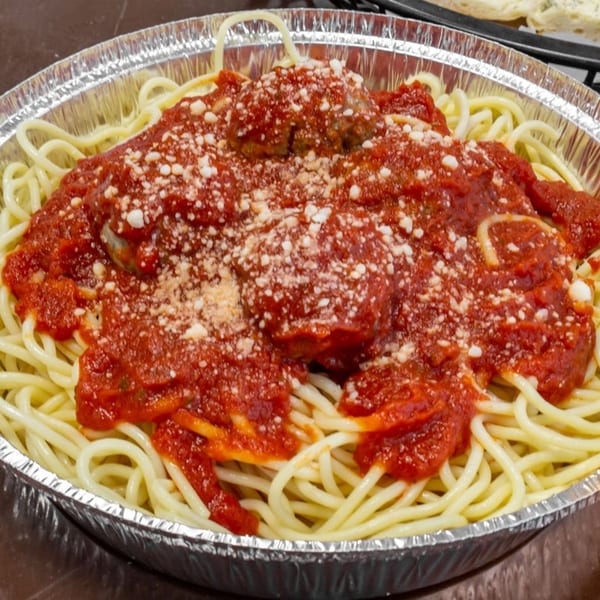 Spaghetti with meatballs and marinara sauce, topped with grated cheese, in a foil container.
