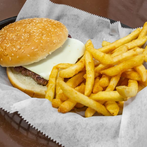 Cheeseburger with a sesame seed bun and a side of golden french fries in a basket.